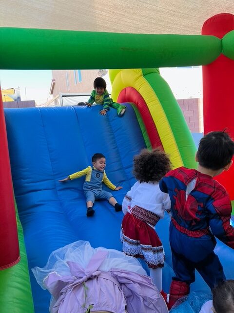 Children joyfully climbing and sliding down an inflatable slide inside a colorful tent.